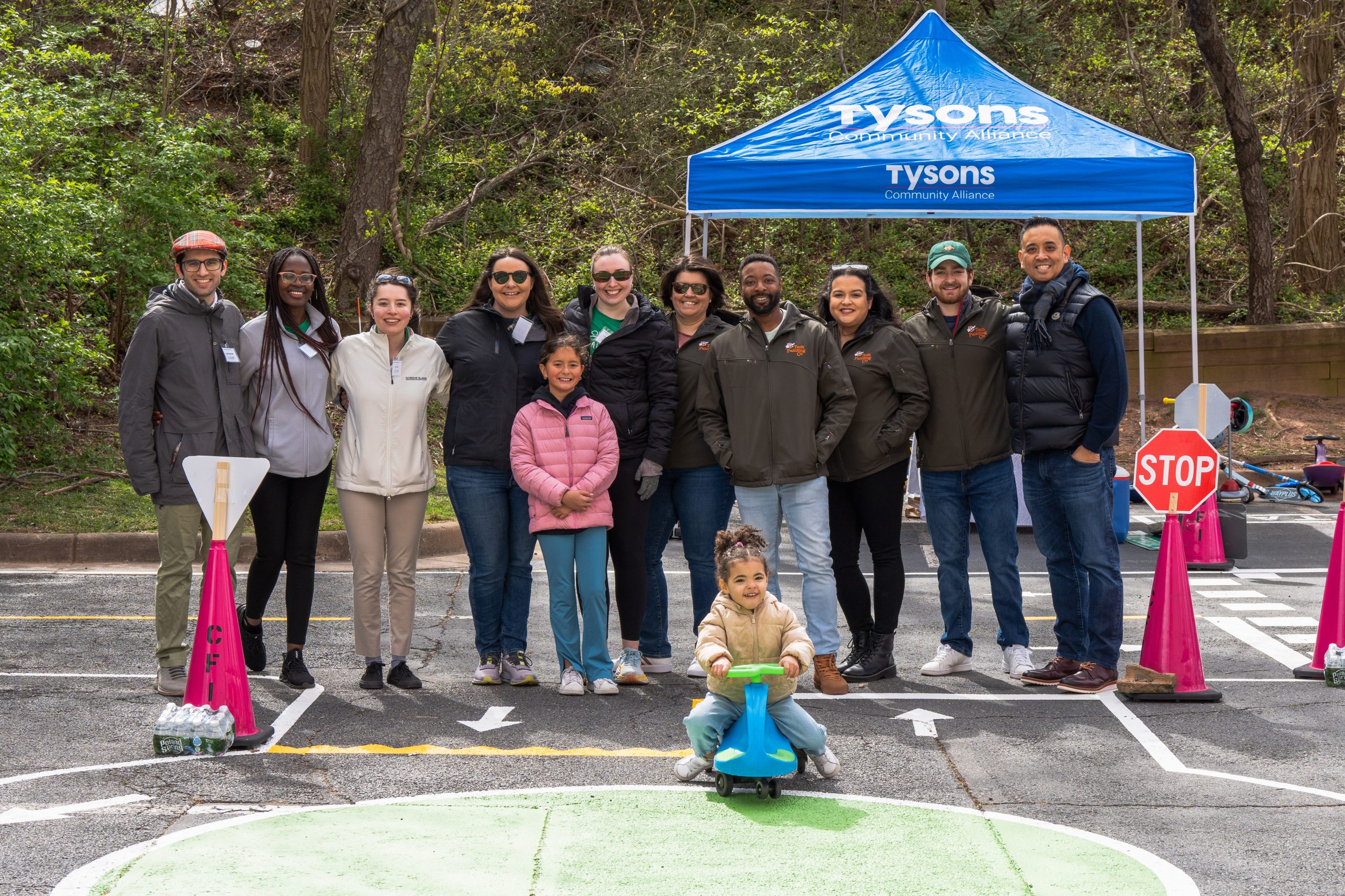 a group of adults stand in front of a blue tent with a toddler in front of them exploring the mobility maze